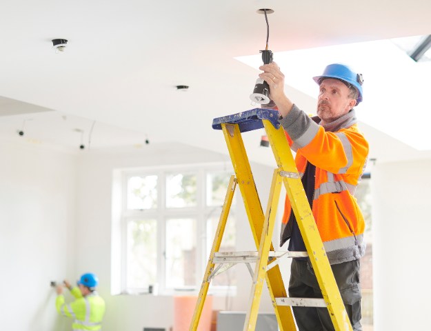 Home rewiring electrician on ladder installing ceiling lights